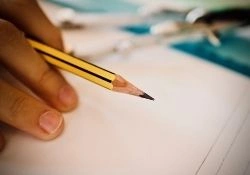 Close-up of a hand holding a sharpened pencil over a blank sheet of paper, ready to write.