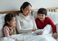 Mother reads a story on a tablet to her two children while they are in bed.
