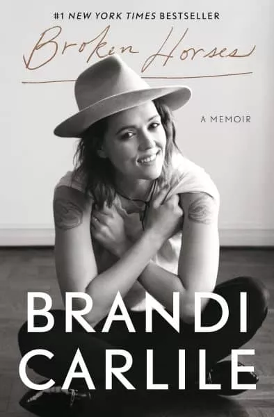 Cover of "Broken Horses: A Memoir" by Brandi Carlile, featuring a black and white photo of the author wearing a hat and