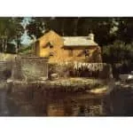 A rustic stone and wood building with laundry hanging on a line in front, situated by a body of water.