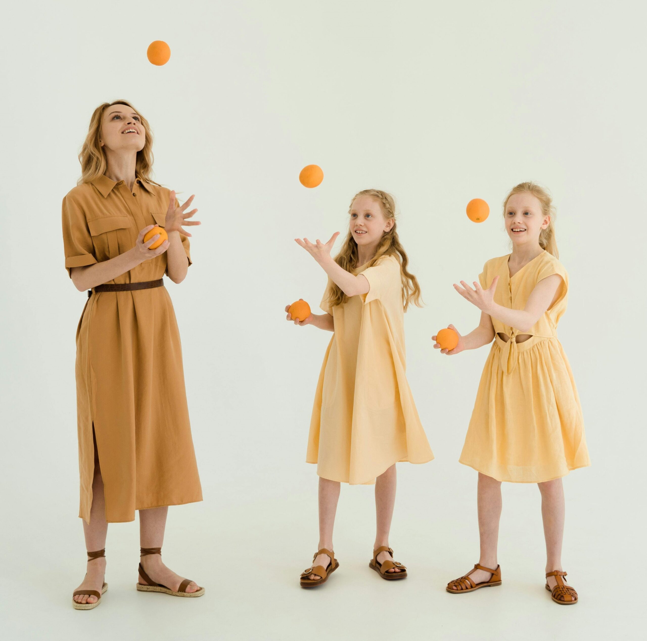 A woman and two girls are juggling yellow balls.